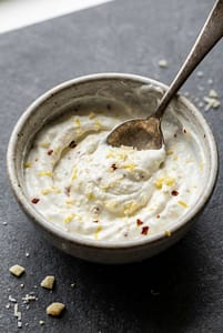 Close-up of creamy Greek yogurt sauce being mixed with parmesan, garlic and lemon zest.