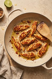Chili lime chicken breast strips cooking in a skillet with garlic, chili flakes, and olive oil.
